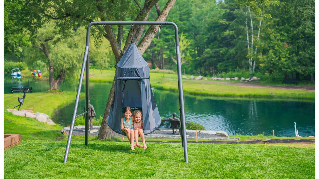 Two kids sitting in a tent swing on a single swing set.