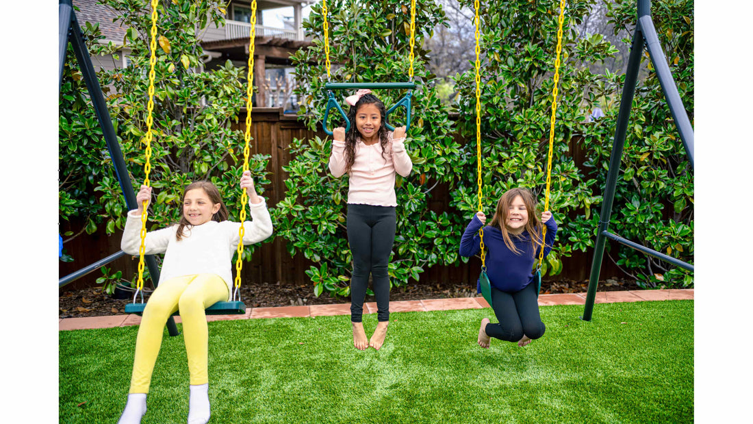 Three little girls smiling while playing on a metal swing set.