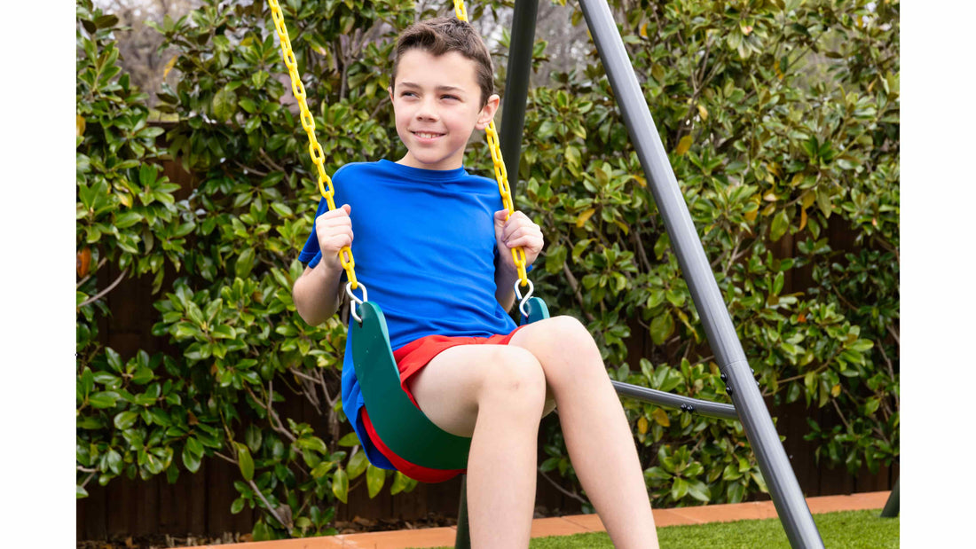 A boy in a blue shirt and red shorts smiling while swinging on a swing set.