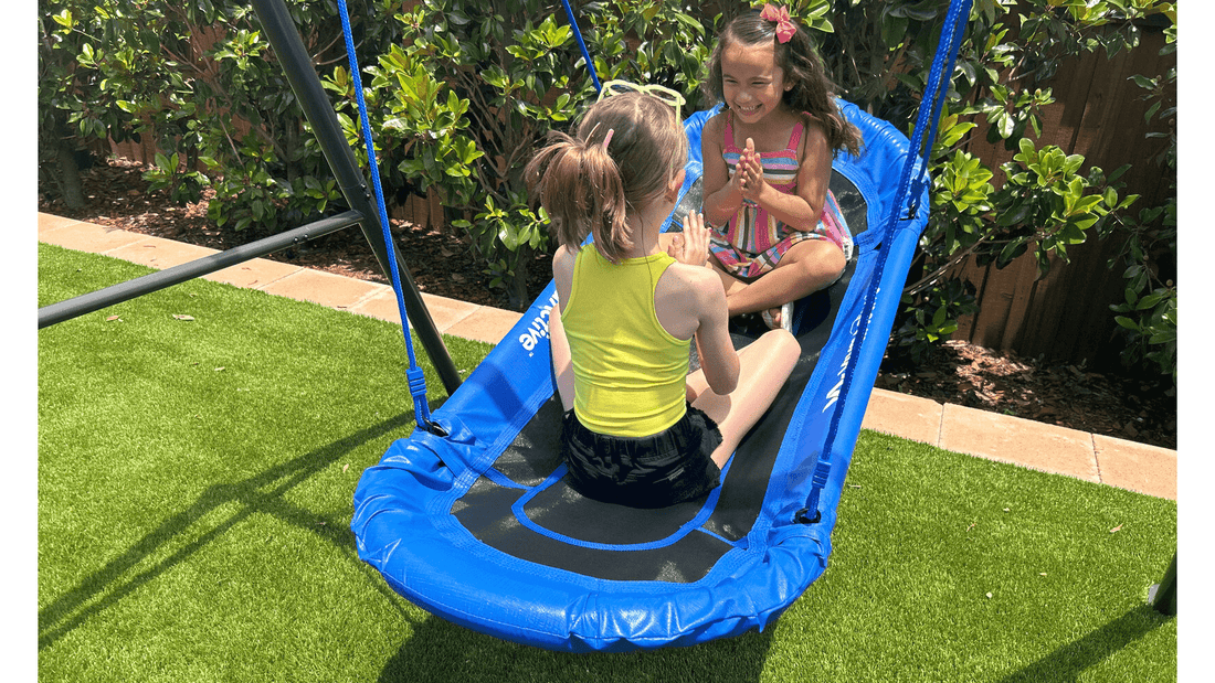 Two little girls playing Pattycake on a blue swing.