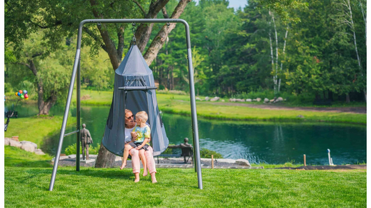 A mother and child sitting in a tent swing on a swing set.