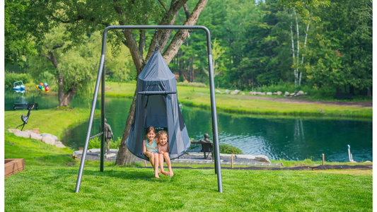 Two kids sitting in a tent swing on a single swing set. 