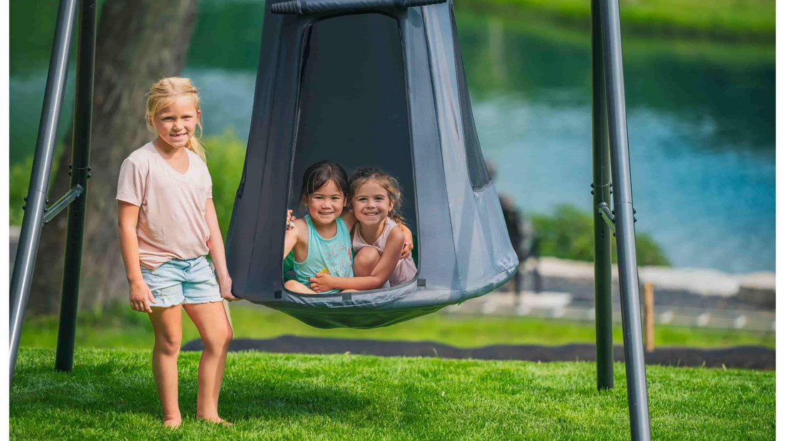Three children standing by or in a tent swing on a swing set.